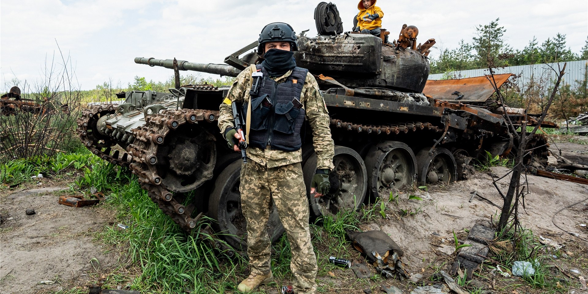Ein ukrainischer Soldat, der hier nach eigenen Angaben gegen russische Einheiten gekämpft hat, steht vor einem zerstörten russischen Panzer, auf dem sein Sohn sitzt.