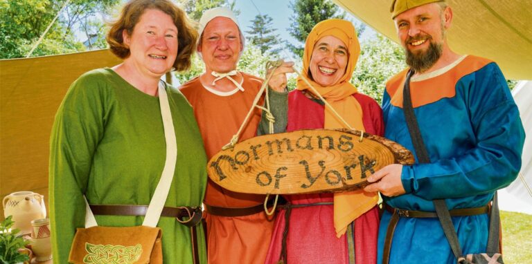 Vier mittelalterlich gekleidete Personen tragen ein Schild mit der Aufschrift „Normans of York“.