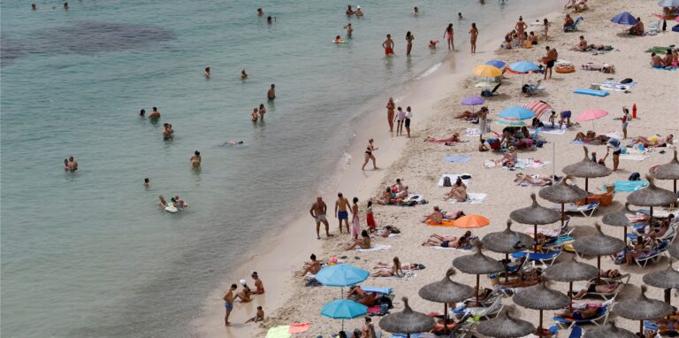 Touristen genießen an einem Strand bei Puerto Portals auf Mallorca die Sonne und das Meer.