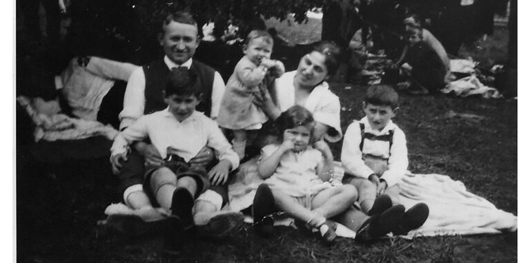 Eine Familie sitzt auf einer Wiese auf einer Decke, historische Schwarz-Weiß-Aufnahme.