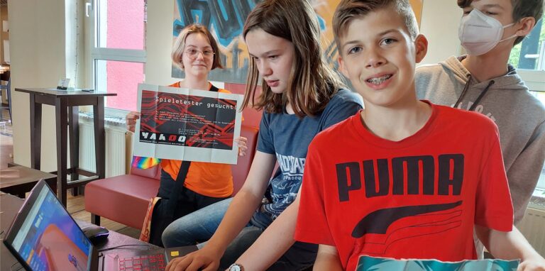 Eine Gruppe von Kindern, einer sitzt am Laptop, zwei halten Plakate hoch.
