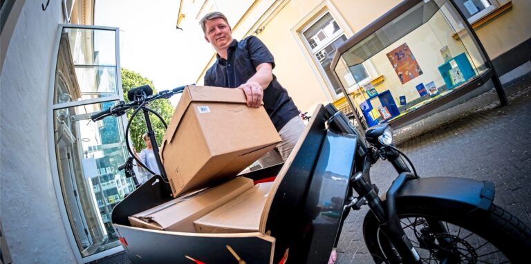 Ein Mann bepackt ein Lastenrad mit Pappkartons.
