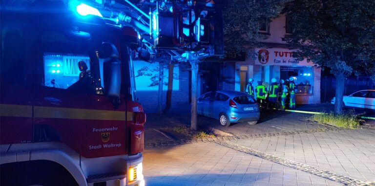 Im Dunkeln steht ein Feuerwehrfahrzeug mit Blaulicht vor einer Häuserzeile in Waltrop.