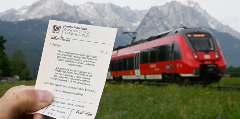 Ein Mann hält ein 9-Euro-Ticket in der Hand, im Hintergrund fährt ein Zug der Deutschen Bahn vor der Bergkulisse des Wettersteingebirges vorbei (gestelltes Foto).