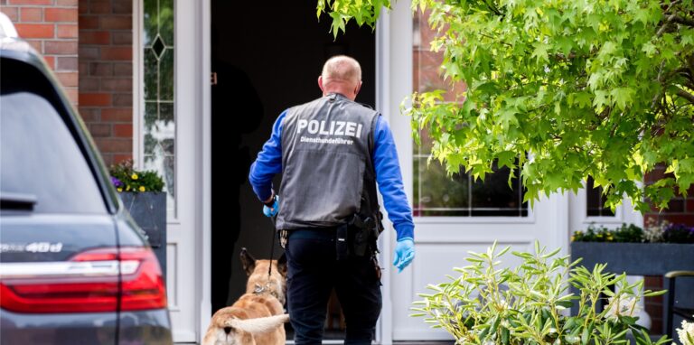 Ein Diensthundeführer der Polizei geht mit einem Spürhund zu einem Wohnhaus, das von Ermittlungsbeamten der Polizei durchsucht wird. Wegen des Verdachts auf bandenmäßigen Betrug mit Corona-Soforthilfen in Millionenhöhe durchsucht die Polizei seit Dienstagmorgen 25 Objekte in vier Bundesländern.