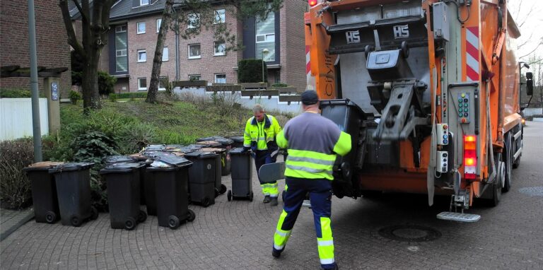 Zwei Mitarbeiter der Müllabfuhr stehen hinter einem Müllwagen.