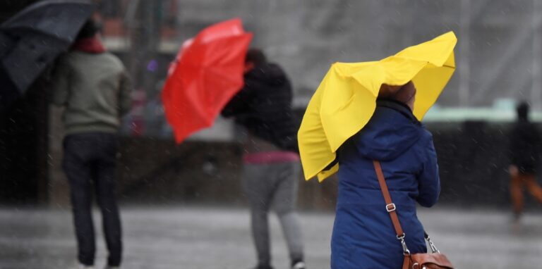 Fußgänger kämpfen bei Wind mit ihren Regenschirmen.