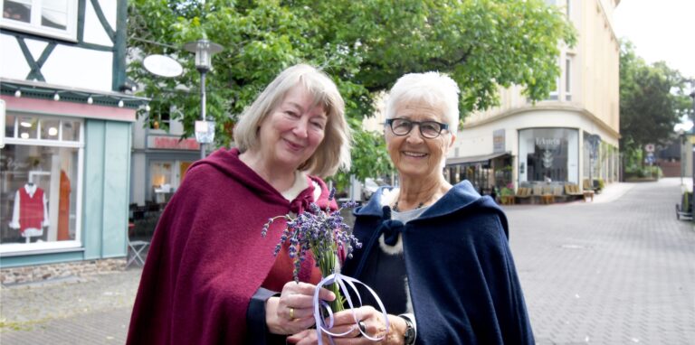 Zwei Frauen in mittelalterlich anmutenden Gewändern stehen vor einem Fachwerkhaus.