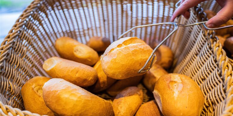 Eine Verkäuferin nimmt ein Brötchen mit einer Zange aus einem Brötchenkorb.