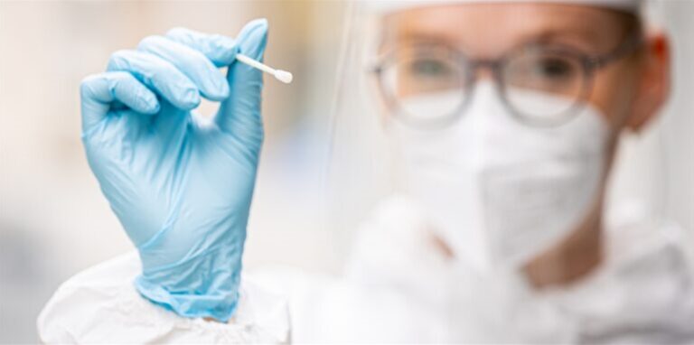 Eine Person in Schutzmontur hält einen Tupfer für einen Coronatest.