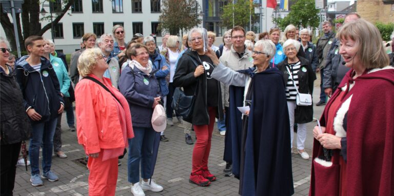 Eine Menschengruppe und zwei Frauen in historischen Gewändern stehen auf dem Rathausplatz in Recklinghausen.