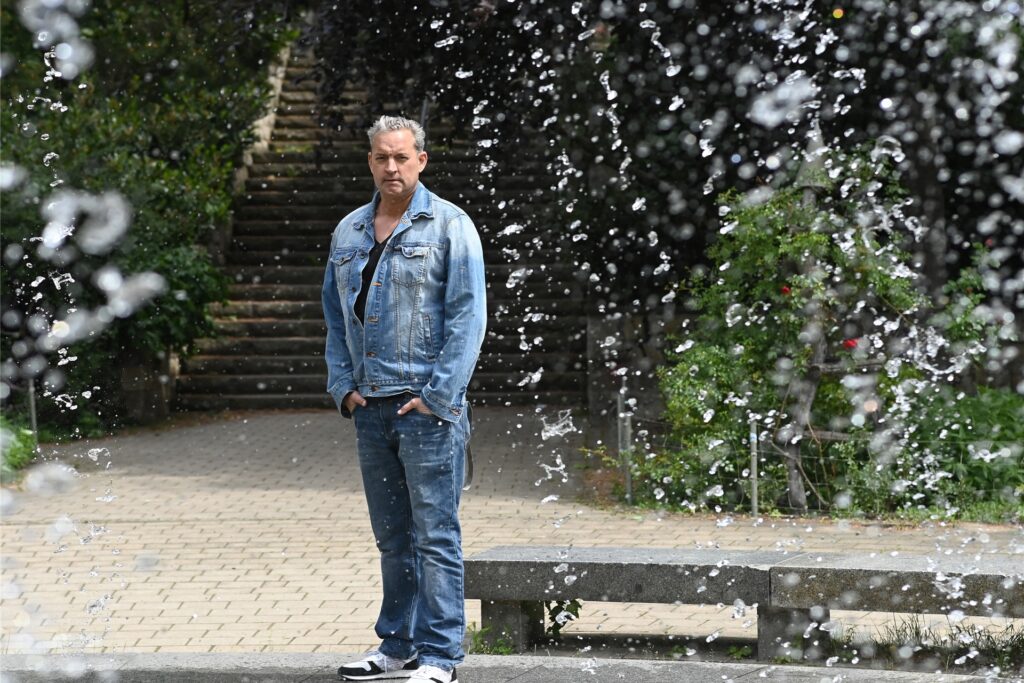 Der Schauspieler Christian Kahrmann steht hinter einem Brunnen in Prenzlauer Berg. 