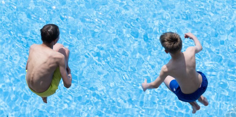 Zwei Jungen springen im Freibad Zacke vom Beckenrand ins Wasser.