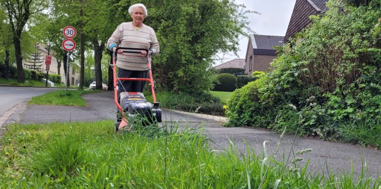 Eine Frau mit einem Rasenmäher auf einem Grünstreifen