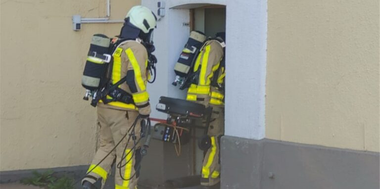 Feuerwehrleute unter Atemschutz tragen Gerätschaften in ein Gebäude.