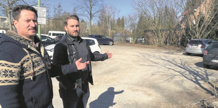 Sergej Tarde (links) und sein Sohn Dennis stehen auf dem Lehrerparkplatz an der Gartenstraße und deuten auf die Fläche, die laut bisheriger Planung für die neue Flüchtlingsunterkunft angedacht ist. Direkt dahinter steht ihr Eigenheim.