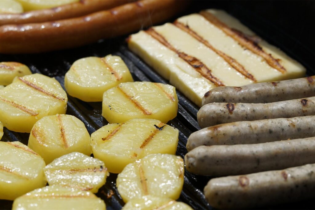 Auf dem Grillrost brutzeln Kartoffeln, Würstchen und Grillkäse
