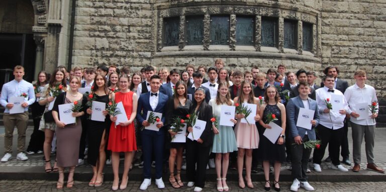 Elegant gekleidete junge Menschen mit Zeugnissen und Rosen haben sich zum Gruppenfoto aufgestellt.