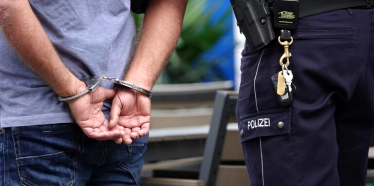 Ein Mann steht in Handschellen neben einem Polizisten.