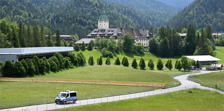 Ein Polizeiauto fährt die Straße von Schloss Elmau herunter, links ist der Pressebereich und rechts die Pressetribüne zu sehen.