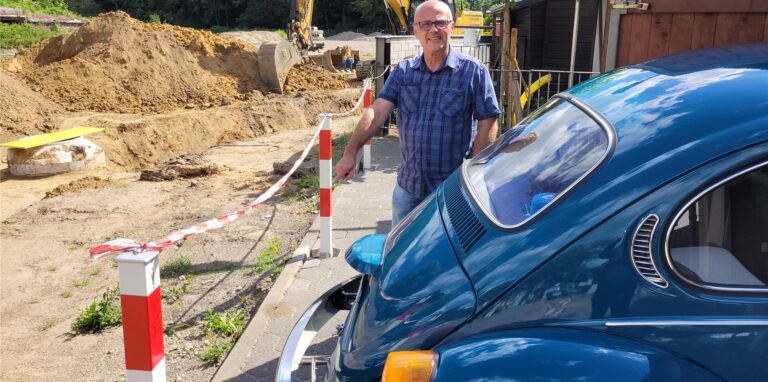 Ein Mann steht hinter seinem Auto an einer Baustelle.