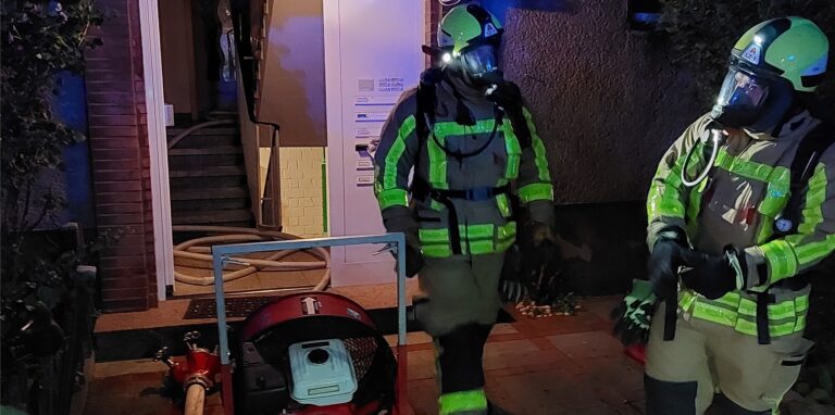 Zwei Feuerwehrleute stehen vor einem Haus.