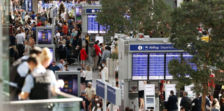 Passagiere stehen im Flughafen Düsseldorf in Schlangen und warten auf ihre Abfertigungen.