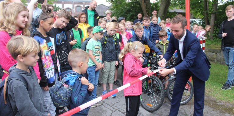 Ein Mädchen und Waltrops Bürgermeister Marcel Mittelbach schneiden gemeinsam symbolisch das Flatterband zum Ferienspaß 2022 auf. Im Hintergrund eine Schar von wartenden Kindern.