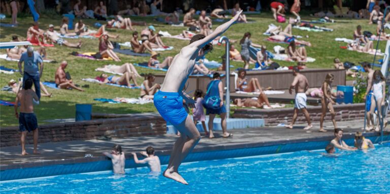 Ein junger Mann springt in das Becken eines Freibads.