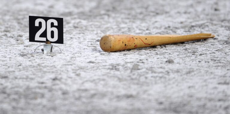 Ein Baseballschläger aus Holz liegt auf einer steinernen Oberfläche, links daneben ein Schild der Kriminaltechnik mit der Ziffer 26.