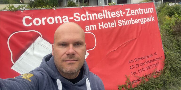 Ein Mann steht vor der Werbung für eine Corona-Teststelle