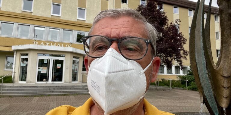 Ein Mann mit Maske steht vor dem Rathaus
