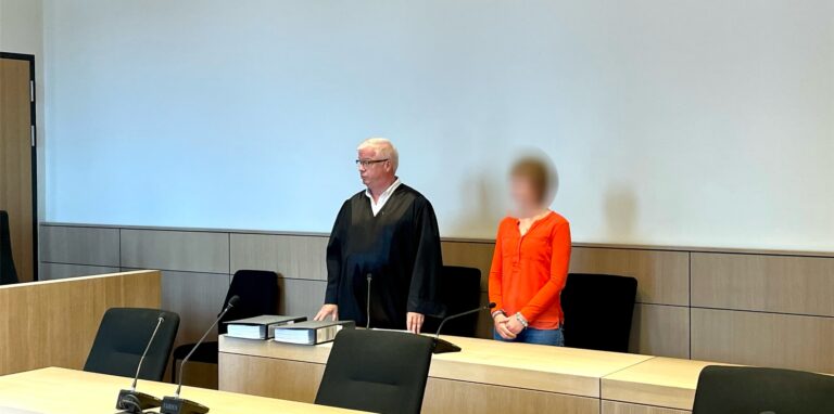 Ein Mann in schwarzer Anwaltsrobe und eine zierliche Frau stehen in einem Gerichtssaal.