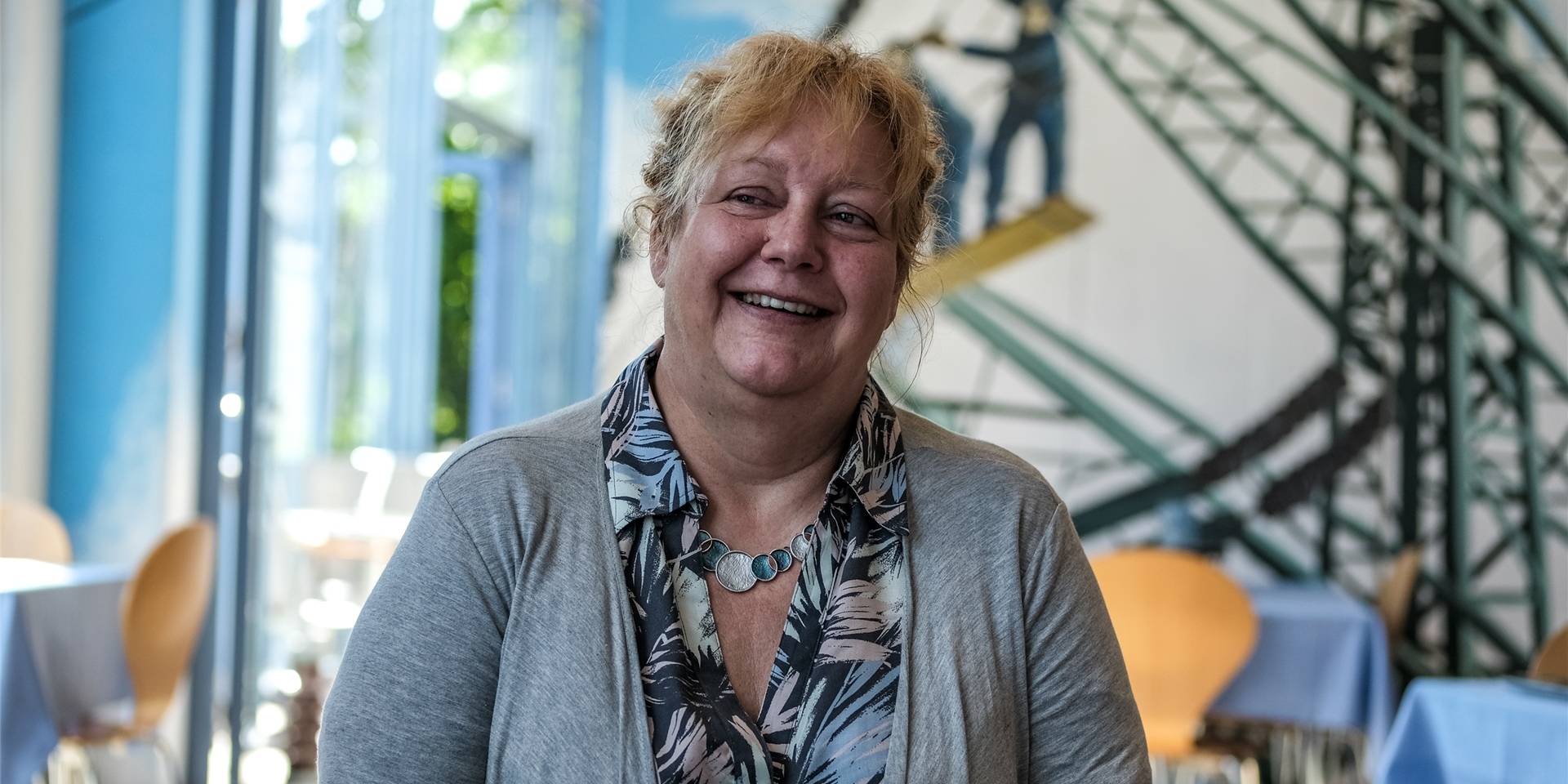 Eine Frau steht vor einer Wand mit aufgebrachtem Strommasten-Motiv.