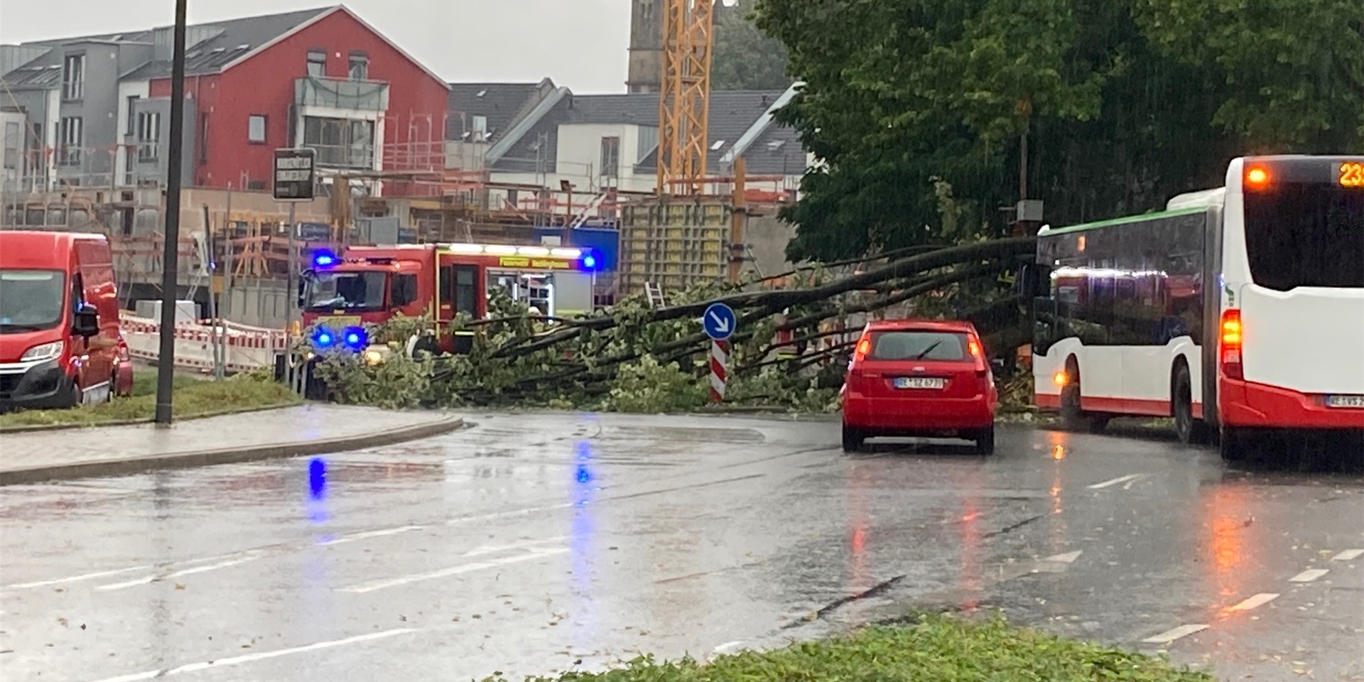 Ein Baum ist auf eine Fahrbahn gestürzt. Rechts ist ein Linienbus der Vestischen zu sehen, im Hintergrund ein Einsatzfahrzeug der Feuerwehr.