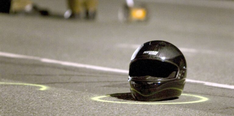 Ein Motorradhelm liegt auf einer Straße, daneben sind Fahrbahnmarkierungen zu erkennen.