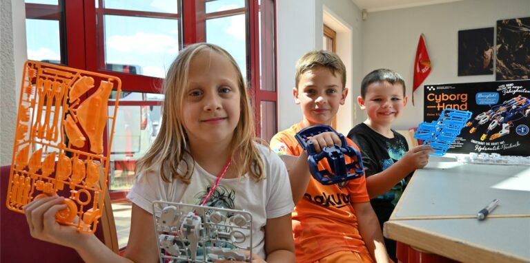 Ein Mädchen und zwei Jungen halten im Jugendtreff in Oer-Erkenschwick die Bauteile für eine Roboter-Hand in die Kamera. Sie lernen beim Ferienprogramm Star Akademie viel über Technik und den Weltraum.