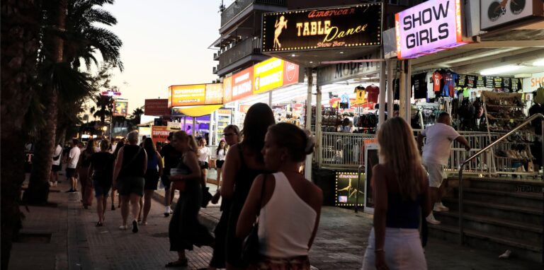 Menschen spazieren auf der Strandpromenade von Arenal auf Mallorca an Show-Bars vorbei.