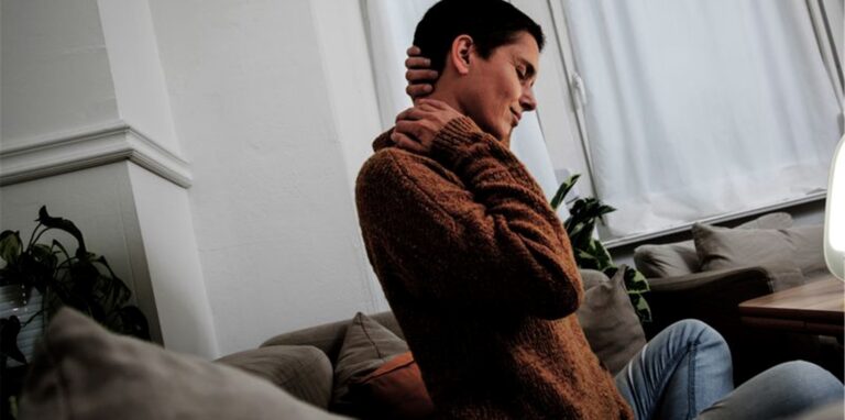 Eine Frau sitzt auf dem Sofa und hält sich den Nacken.