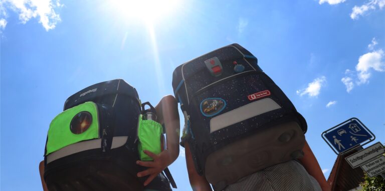 Zwei Kinder laufen mit ihren Büchertaschen im Sonnenschein.