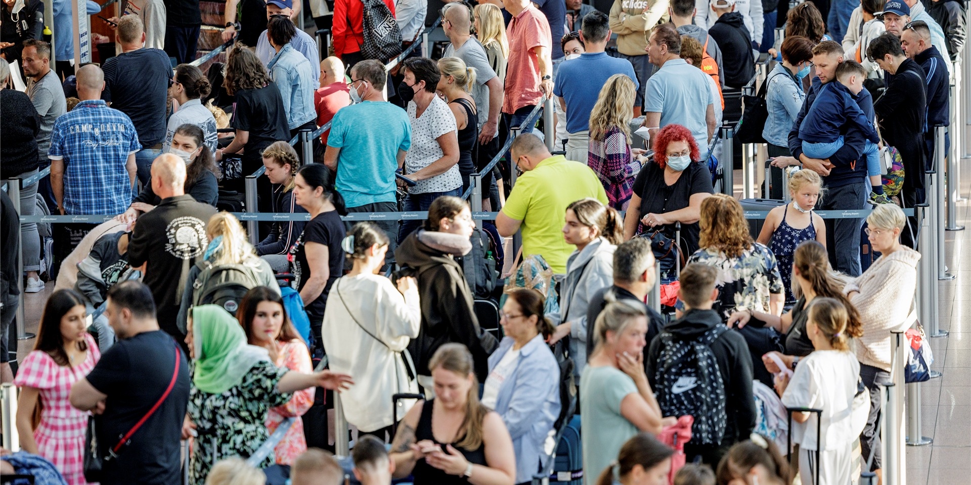 Fluggäste warten im Flughafen vor den Check-In Schaltern auf die Abfertigung.
