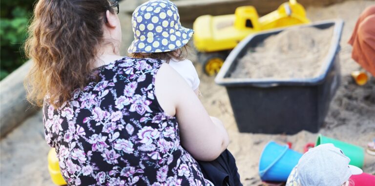 Eine Betreuerin sitzt in der Kindertagesstätte Kita Morgenland mit Kindern an einem Sandkasten.