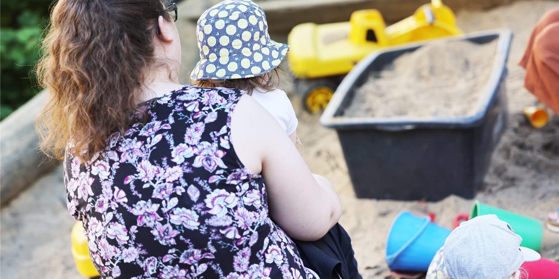 Eine Betreuerin sitzt in der Kindertagesstätte Kita Morgenland mit Kindern an einem Sandkasten.