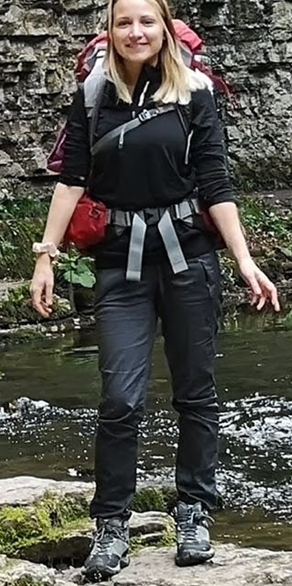 Das Bild zeigt eine junge Frau mit langen, dunkelblonden Haaren in Wanderkleidung und mit einem Rucksack.