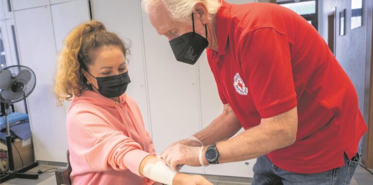 Ein Mann legt am Arm einer Frau  beim DRK in Oer-Erkenschwick einen Verband an.