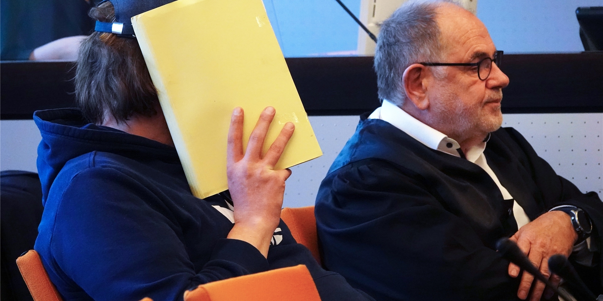 Einer der beiden Angeklagten (l), der sich im Saal des Landgerichts eine Mappe vor das Gesicht hält, sitzt neben seinem Anwalt.