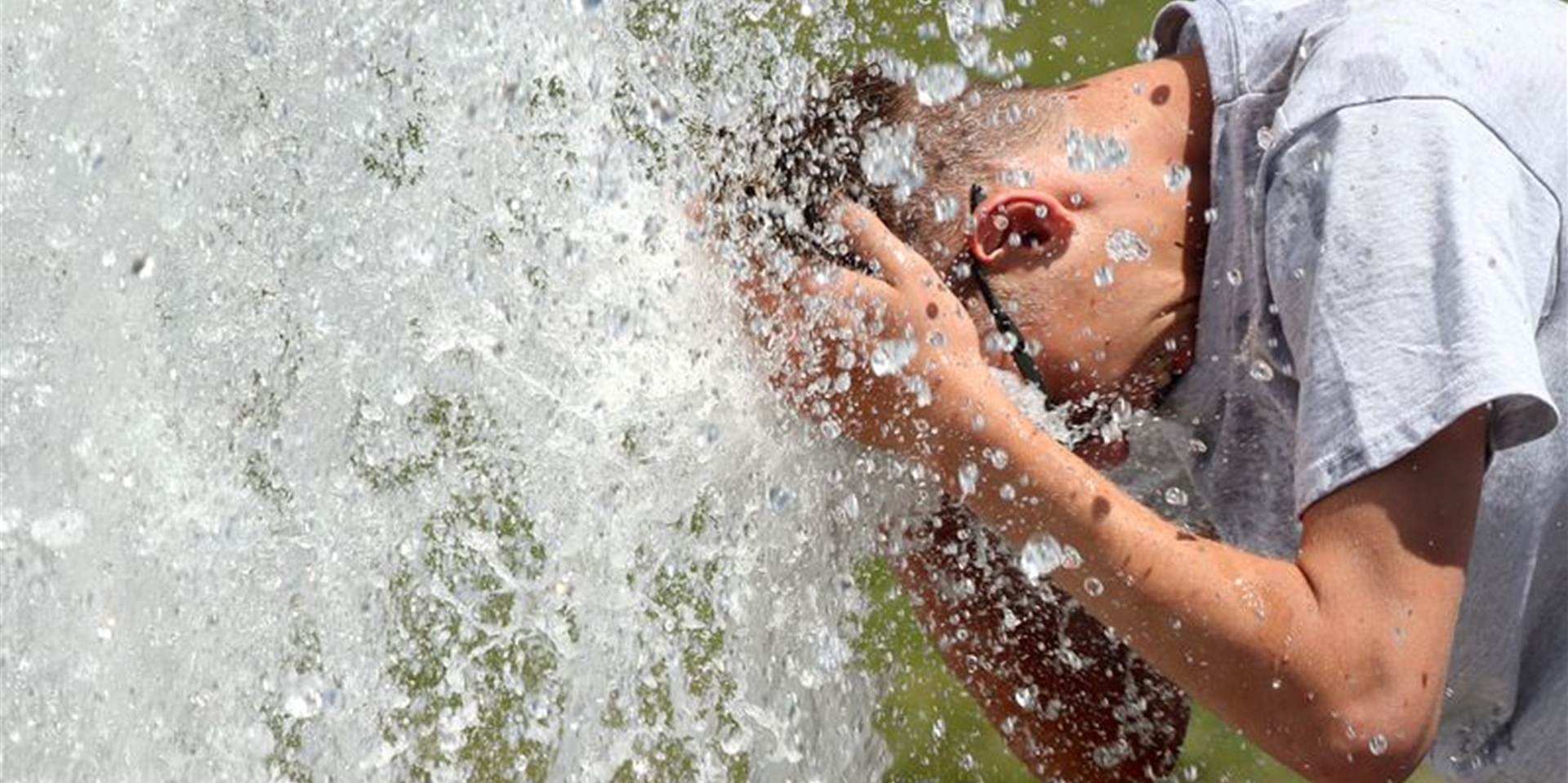 Bei Temperaturen um 29 Grad Celsius erfrischt sich ein junger Mann im Berliner Lustgarten am Wasser eines Brunnens.