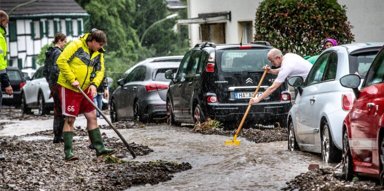 Anwohner in Hagen leiten bei Aufräumarbeiten an einer Straße im Ortsteil Hohenlimburg das ablaufende Wasser. Hier hatte Starkregen für teilweise chaotische Zustände gesorgt.
