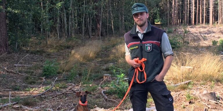 Revierförster Lennart Besten steht im Wald mit seinem Hund.