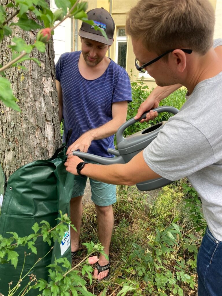 Zwei Männer füllen einen Gießsack an einem Baum in Recklinghausen mit Wasser Zwei Männer füllen einen Gießsack an einem Baum in Recklinghausen mit Wasser